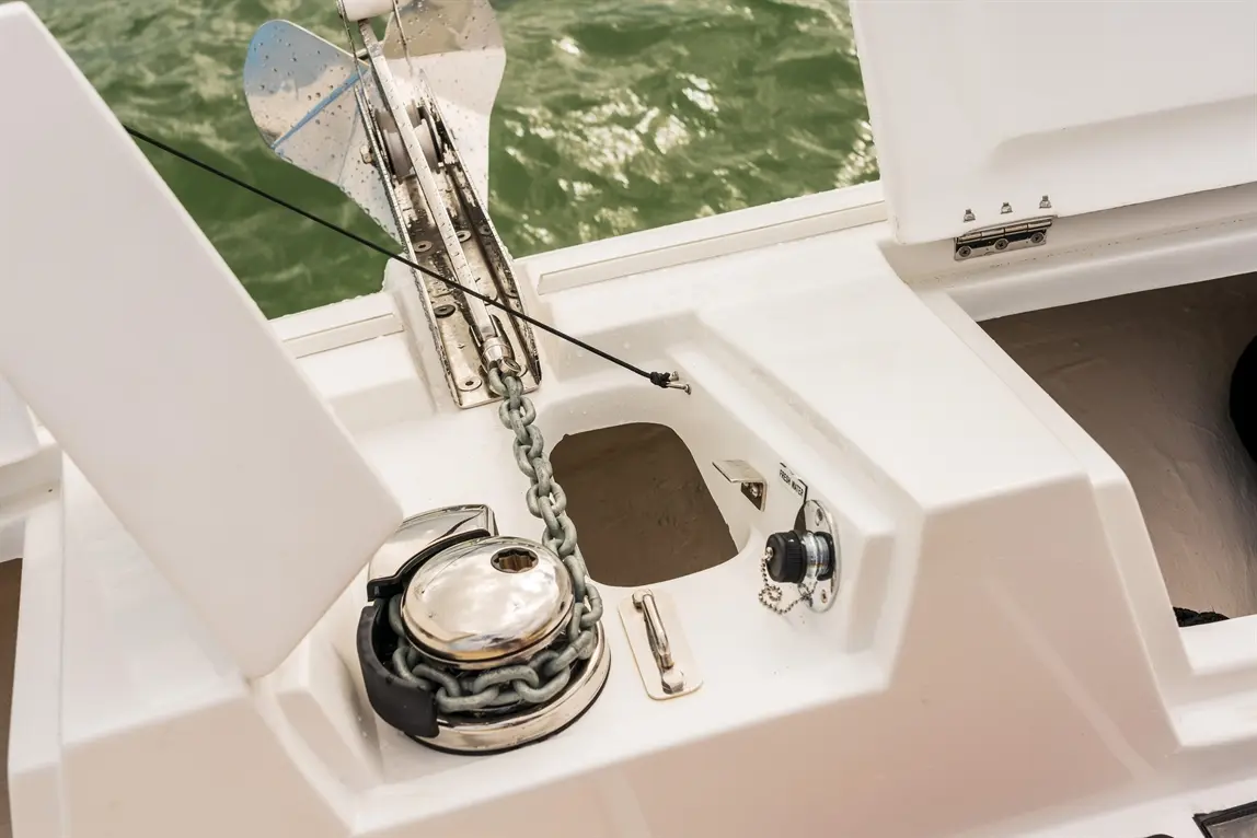 Boat anchor mechanism featuring a stainless steel winch, chain, and compartment, set against a green water background.